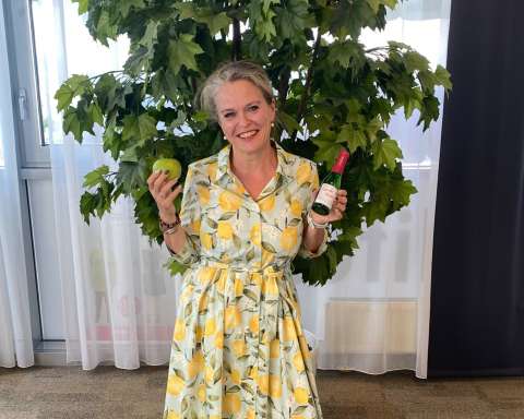 Silvia Boschak lächelt im Kleid mit Zitronenmuster und hält einen Apfel und eine Flasche in den Händen.